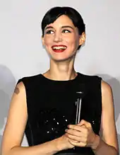 A smiling woman with short hair wears a black dress.lol