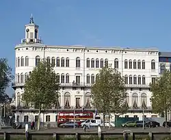 White building of four stories with a small tower on the top, green trees in the front