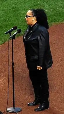 A woman wearing a black suit while at the microphone