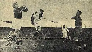 An action shot from a football match. A goalkeeper jumps and catches the ball.