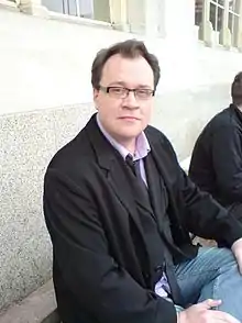 Davies outside Cardiff Central railway station, sitting with his back towards a marble-effect wall.