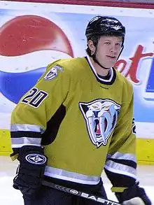 An ice hockey player skates on the ice. He is wearing a gold jersey with an image of a sabertooth tiger on the front.