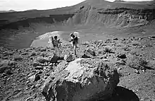 Two people in astronaut-like clothing next to a deep crater