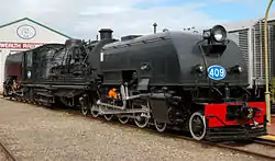 Front oblique view of a black steamtrain with a blue-and-white number 409 on the front and a large shed visible behind