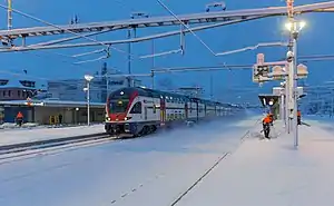 Double-decker train passes through snow-covered platforms