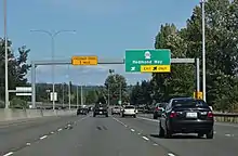 A four-lane freeway separated from oncoming traffic by a concrete barrier. A sign in the background indicates that the exit for State Route 202 is approaching.