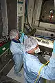 Workers in protective clothing inspect and clean the interior of Node 3