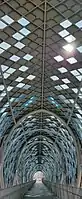 An interior shot of the Saloma Link footbridge in Kuala Lumpur, showing the complex steel lattice structure interspersed with cladding and glass panels.