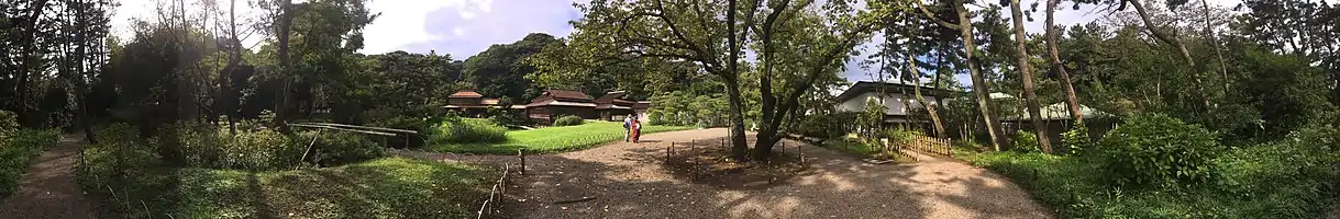 Panorama view from inside Sankei-en showing people on walking paths among green trees.