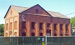 Two-story brock building with boarded windows and fence in foreground