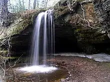 A rock outcropping overhanging a small pool of water with a waterfall cascading into the pool