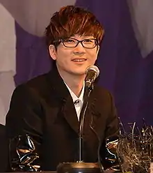 Seo Taiji sits at a table with a microphone on it.