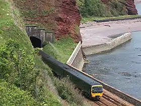 A train outside a tunnel with a beach and breakwater on the right