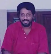 Upper-body photo of smiling man with dark hair, moustache and beard wearing dark-coloured button down shirt