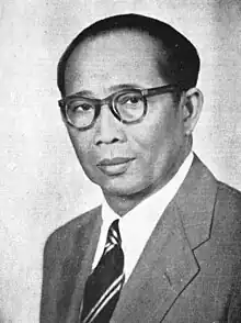 Black-and-white portrait of Sidik Djojosukarto wearing a suit-and-tie and round-framed glasses