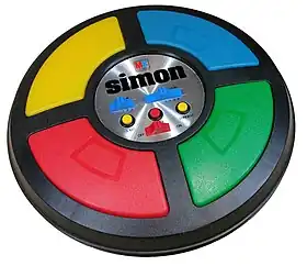 The game is a circular disc divided into four quarter circle buttons each with a different color. In the center are the game mode controls