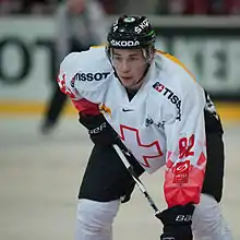 A Caucasian male ice hockey player shown from the knees up. He is wearing a red and white sweater with a black helmet.