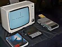 ZX81 in between a copy of the "ZX81 BASIC Programming" manual and a cassette tape recorder, with a black-and-white Ferguson TV set on the background.