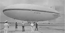 An airship standing on an airfield with several people looking at it