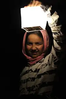 14 year old Syrian refugee girl at night dressed with a head scarf is illuminated by holding up a Solar lantern called SolarPuff in the Idomeni refugee camp in Greece 2015