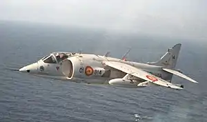 A Harrier flies over an aircraft carrier below.