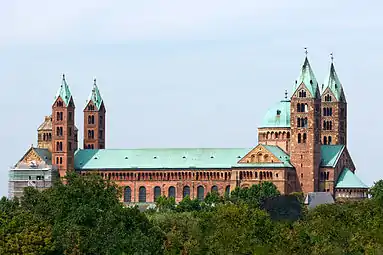 An enormous cathedral, of red stone with green copper roofs, has a two tall towers framing an octagonal dome at each end of the building.