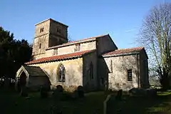 A stone church with red tiled roofs seen from the southeast, showing the chancel, the south aisle, clerestory and porch, and the tower plain parapet