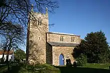 A stone church seen from the south with, on the left, an embattled tower with pinnacles, and to the right a nave with clerestorey, aisle, and pointed doorway