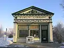 The small facade of St. Bonifacius, a white building with two columns and green and gold ornamentation, on a sunny winter day.