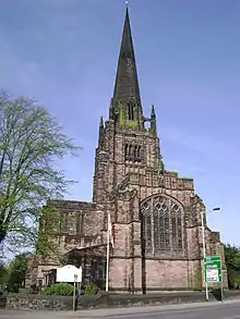 An elaborate Gothic Revival church seen from the west, with a central tower surmounted by a tall spire