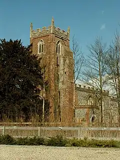 A brick tower with a battlemented parapet, and the body of the flint church beyond it