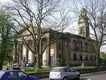 A Neoclassical church with a portico supported by six columns, and clock tower surmounted by an open lantern with columns