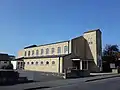 Our Lady of Mount Carmel and St Wilfrid's Church, Selsey. A brick-built church with a small tower, taken from the road, against a blue sky.