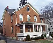 A two-and-a-half-story brick house with cross-gables, decorative window lintels and a white wooden porch