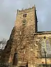 A stone church seen from the south-east with a square, battlemented tower to the left. Part of the body of the church can be seen extending to the right.