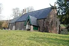 Stone building with small bell tower. In the foreground are gravestones.