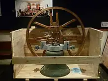 Photo of a large metal bell and its circular wooden support in a half unpacked crate