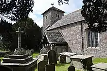 A square base of three stone steps supporting a stone block and simple cross, surrounded by gravestones and tombs