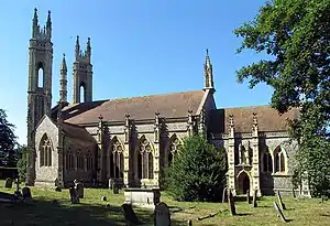 A photograph of a building with several windows standing on a field of green grass containing tombstones all under a clear blue sky