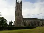 A Gothic church with a tall west tower surmounted by a complex parapet and pinnacles