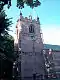 A sandstone church tower seen from a low angle with part of a tree to its left