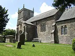 Grey stone building with square tower. Foreground is grass with gravestones.