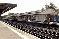 A grey railway platform with a railway track running down the middle and a rectangular, red sign reading "WHISTLE" in white letters