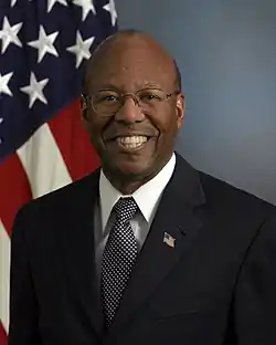 Undersecretary Stanley, wearing eyeglasses, dark blue suit with flag pin in his lapel