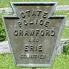 A commemorative cemetery marker with the emblem of the State Police of Crawford and Erie Counties