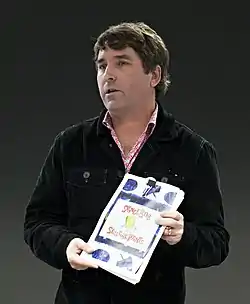 Stephen Hillenburg stands holding a book looking off to his right.