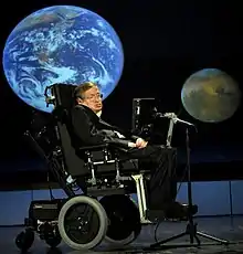 A man in a wheelchair sits in front of an image of Earth and an image of Mars.