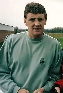 A man with brown hair, wearing a light green sweater and looking slightly to his left