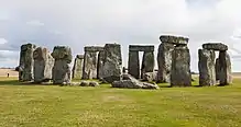 Sun shining through row of upright standing stones with other stones horizontally on the top.