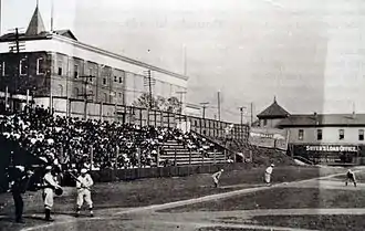 A black and white photograph of home plate and the left field bleachers at a ballpark.